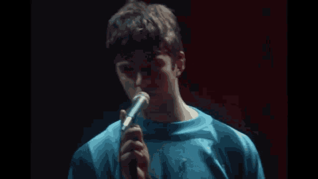 a man in a blue shirt is singing into a microphone on a stage .