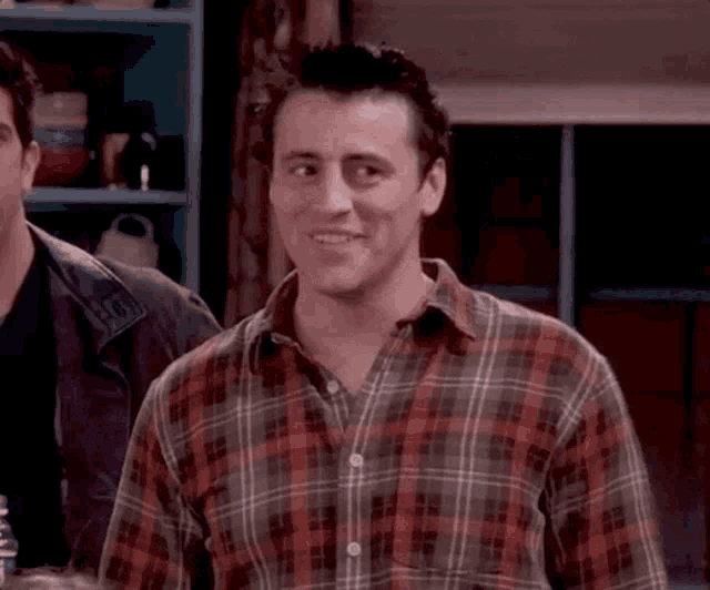 a man wearing a plaid shirt is smiling while standing next to another man .