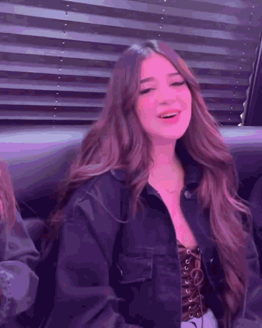 a woman with long brown hair is wearing a black jacket and a purple top .