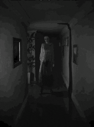 a black and white photo of a woman standing in a dark hallway .