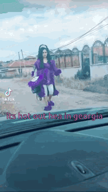 a woman in a purple dress is walking down a street in a car .