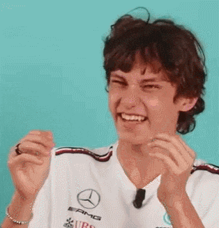 a young man wearing a mercedes shirt is laughing and clapping his hands .