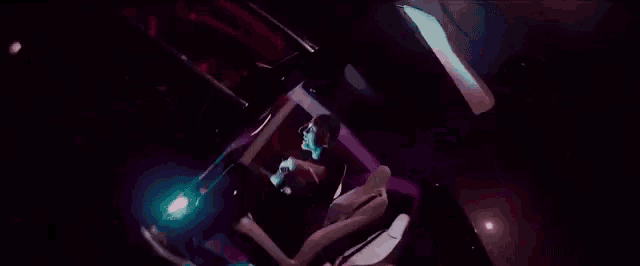 a man is laying on a bed in a dark room with a purple light behind him .