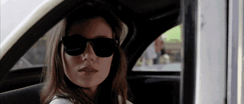 a woman wearing sunglasses looks out the window of a car