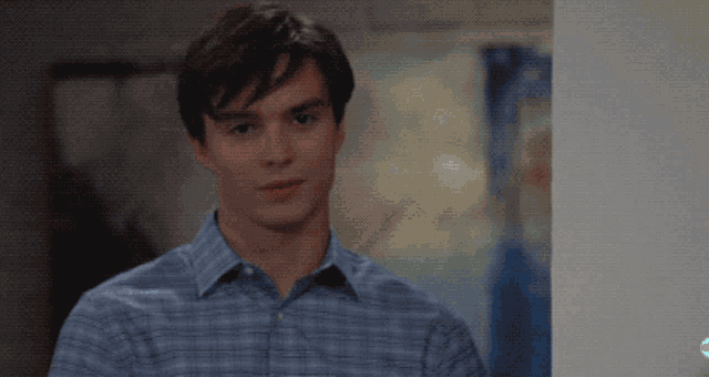 a man in a blue plaid shirt is standing in front of a wall with abc written on it