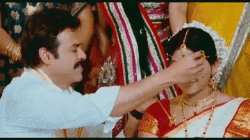 a man is touching a woman 's face in a traditional indian wedding ceremony .