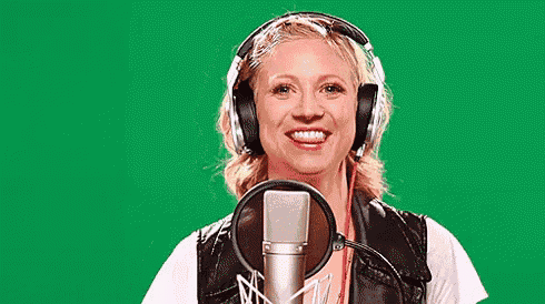 a woman wearing headphones is singing into a microphone against a green screen .