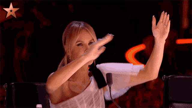 a woman sitting in front of a microphone with her arms in the air