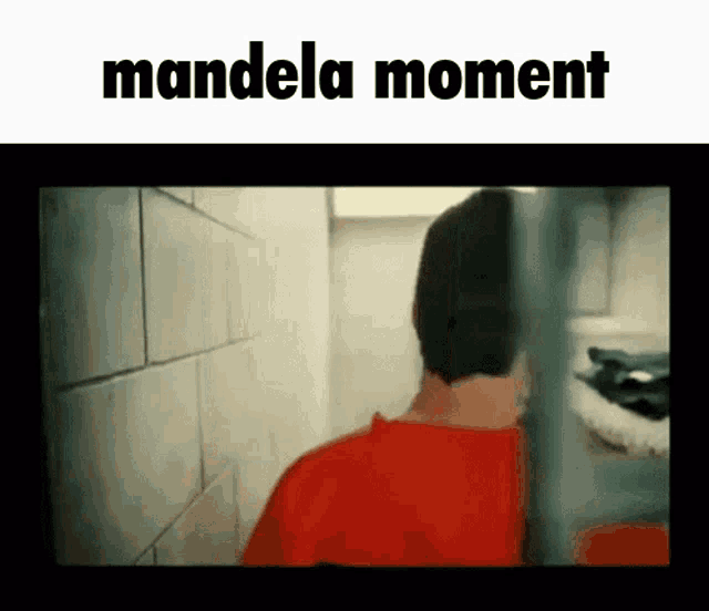 a man in a red shirt is standing in a prison cell with the words mandela moment written above him .