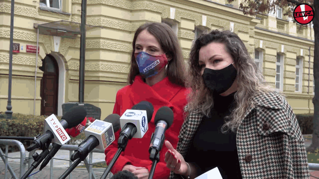 two women wearing face masks are standing in front of microphones one of which says tvp info on it