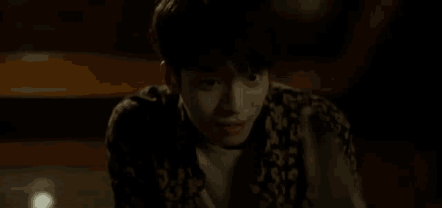 a young man is sitting on the floor in a dark room looking at the camera .