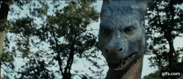 a close up of a dinosaur 's face in front of trees .