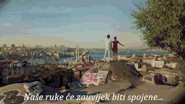 a man and woman are standing on top of a hill overlooking a city