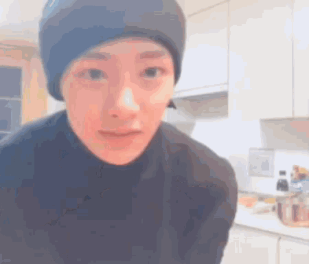 a man wearing a beanie and a black sweater is standing in a kitchen .
