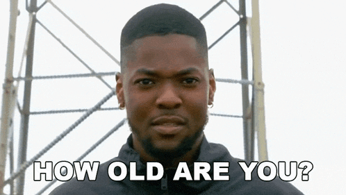 a young man with a beard is standing in front of a scaffolding and asking how old are you .