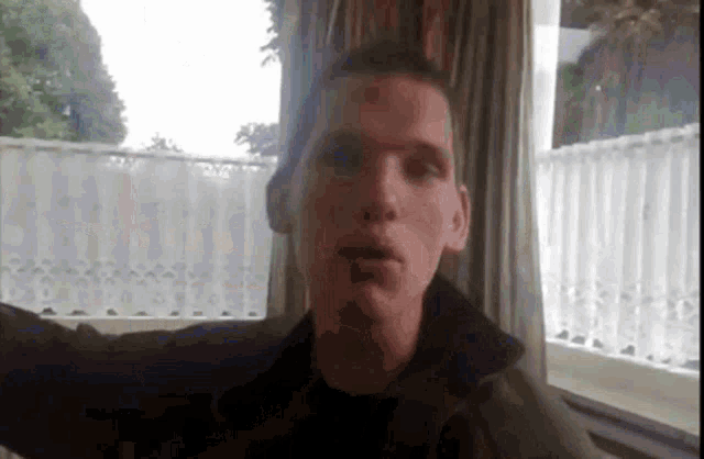 a man in a black jacket is sitting in front of a window with his arms outstretched .