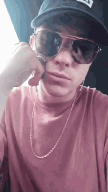 a young man wearing a hat and sunglasses is taking a selfie .