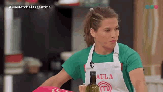 a woman wearing an apron that says aula is standing in a kitchen