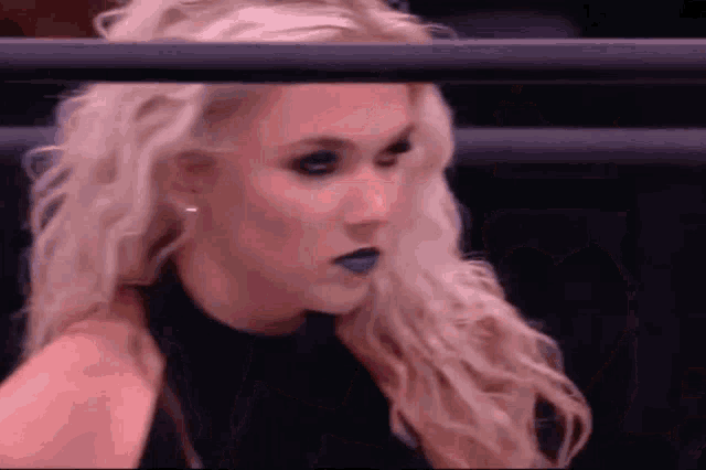 a woman with blonde hair and blue lipstick is sitting in a ring .