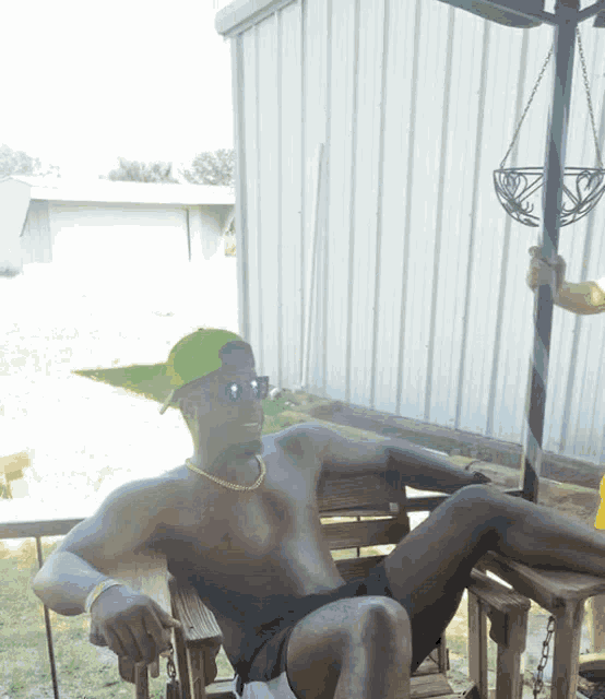 a shirtless man wearing a green hat and sunglasses sits on a wooden bench