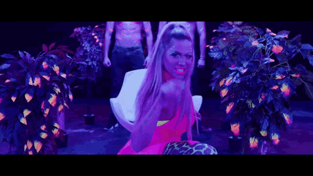 a woman in a neon pink dress is surrounded by glow in the dark plants and says hasta la vista baby
