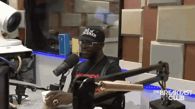 a man is sitting in front of a microphone wearing a hat that says ' hall of fame ' on it