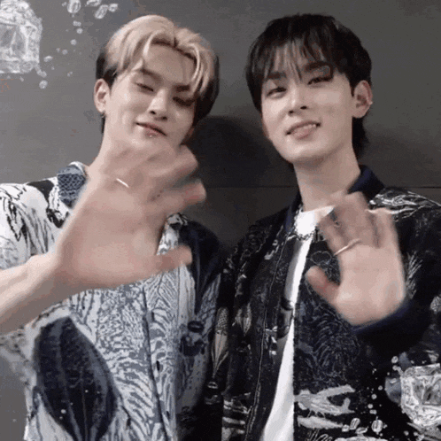two young men are standing next to each other and waving their hands in front of a black wall .