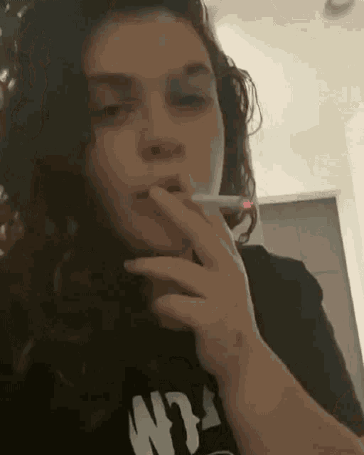 a woman is smoking a cigarette in a room while wearing a black shirt .