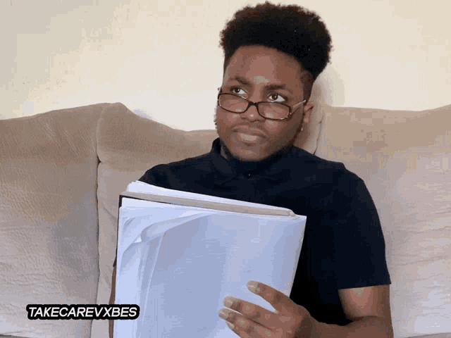a man sitting on a couch reading a book with a takecarevxbes sticker
