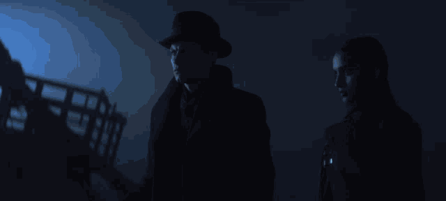 a man in a hat stands next to another man in a black coat