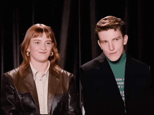 a man and a woman are standing next to each other and the man is wearing a green turtleneck with the word when on it