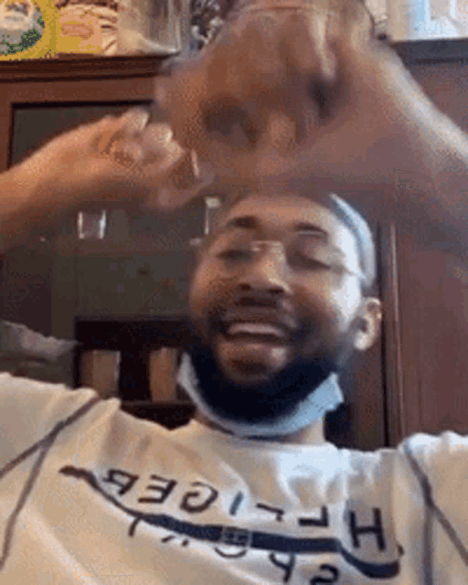 a man wearing a mask and a tommy hilfiger shirt is making a heart with his hands .