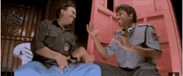 two men are sitting in front of a red door and laughing