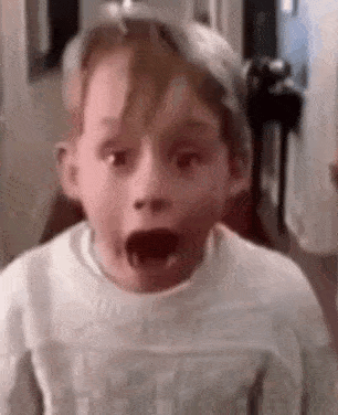 a young boy is making a surprised face while wearing a white sweater .