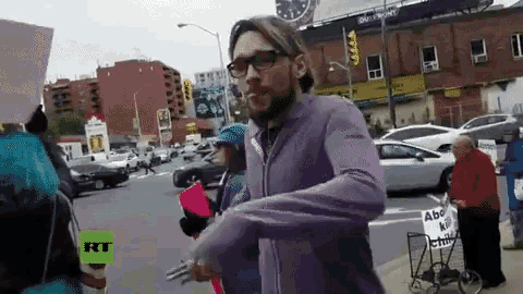 a man in a purple jacket is walking down a street with a rt logo in the background