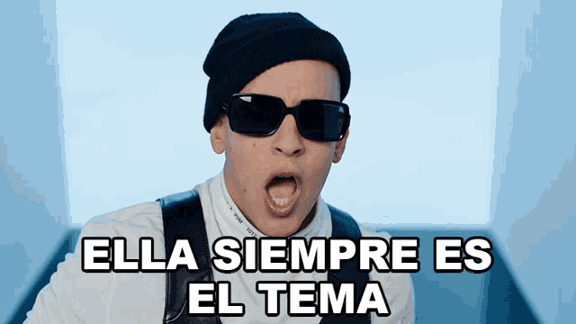 a man wearing sunglasses and a beanie with the words ella siempre es el tema above him