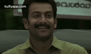 a man with a mustache is smiling and sitting in a car .