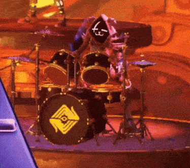 a person is playing drums on a stage with a drum set with a triangle logo on the drum
