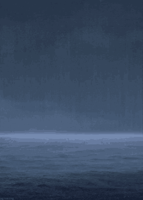 a dark blue ocean with a few waves and a few clouds in the sky