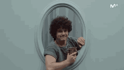 a man with curly hair is holding a cup in a window .