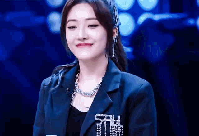 a woman wearing a black jacket and a necklace is smiling .