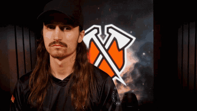 a man with long hair and a hat stands in front of a large logo