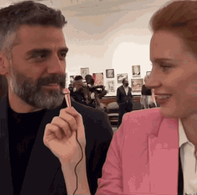 a man with a beard is talking to a woman in a pink jacket while holding a microphone .