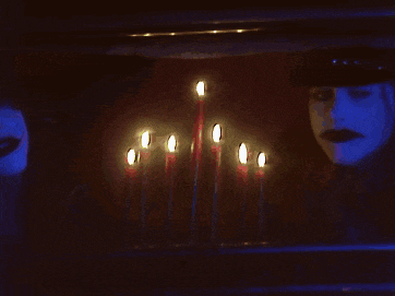 candles are lit up in a dark room with a man in a hat behind them