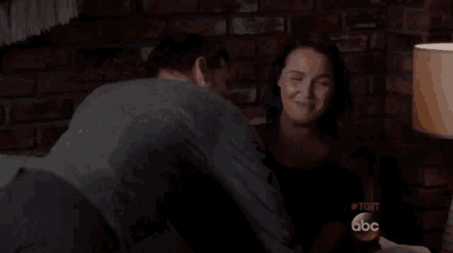 a man and a woman are laying on a bed with a lamp and a brick wall in the background .