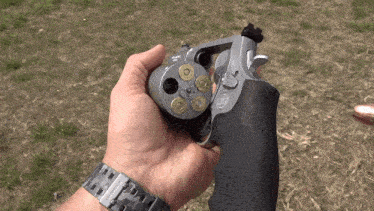 a man wearing a watch is holding a revolver in his right hand