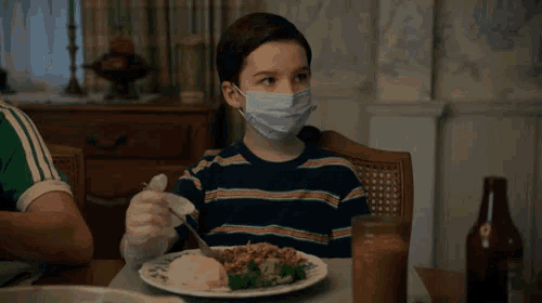 a young boy wearing a mask is eating a meal