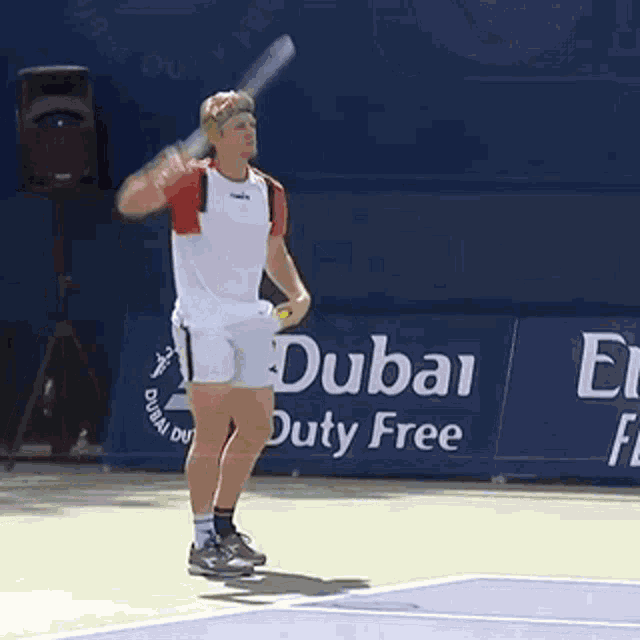 a man swings a tennis racquet in front of a sign that says dubai duty free