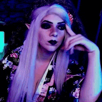 a woman with purple hair and black makeup is sitting in a chair with her hand on her chin .