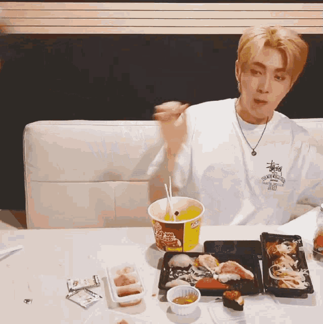 a man wearing a stussy t-shirt is sitting at a table eating food